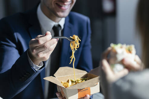 Geschäftsmann isst Nudeln, während er mit einem Kollegen in der Cafeteria im Büro sitzt - JSRF01304