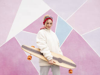 Lächelnde Frau, die ein Skateboard hält und vor einer bunten Wand steht - JCCMF00926