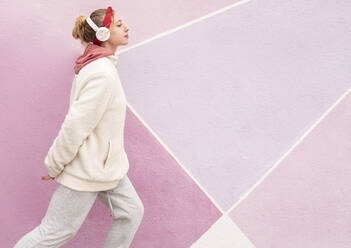 Young woman wearing headphones running against colorful wall - JCCMF00932