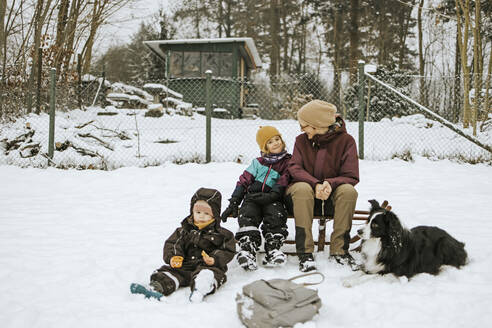 Mutter mit Töchtern und Border Collie auf einem Schlitten sitzend auf einem verschneiten Feld - DWF00568