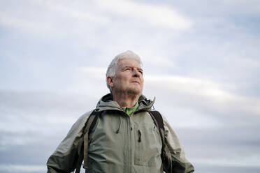 Senior male hiker looking away while standing against cloudy sky during weekend - AFVF08098