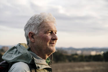 Lächelnder älterer Mann, der bei Sonnenuntergang in die Landschaft blickt - AFVF08104