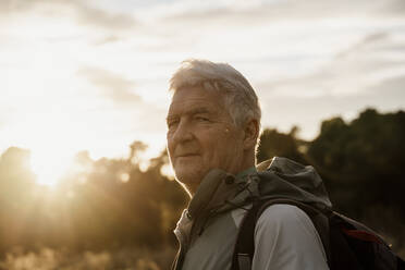 Älterer männlicher Wanderer mit Rucksack vor bewölktem Himmel bei Sonnenuntergang - AFVF08110