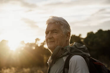 Senior male hiker with backpack against cloudy sky during sunset - AFVF08110