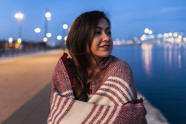 Young woman wrapped in scarf day dreaming by bay of water - JMPF00866