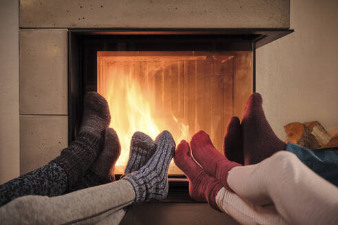 Family warming up feet in woolen socks by fireplace in living room - DIKF00550