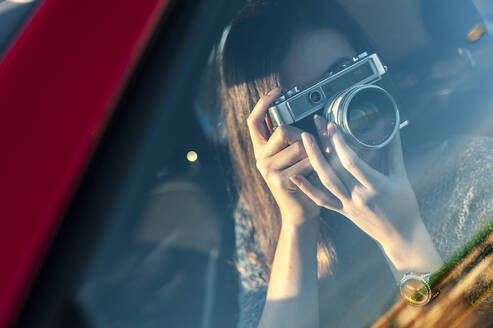 Junge Frau fotografiert mit einer alten Kamera durch ein Glasfenster eines Autos - JMPF00867