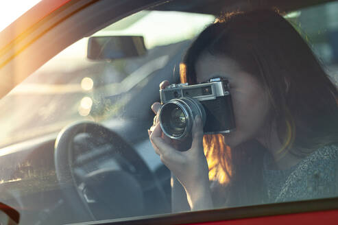 Junge Frau, die vom Auto aus mit einer altmodischen Kamera fotografiert, während sie unterwegs ist - JMPF00868
