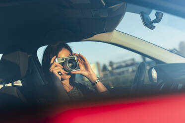 Junge Frau, die am Wochenende mit einer Filmkamera vom Auto aus fotografiert - JMPF00870