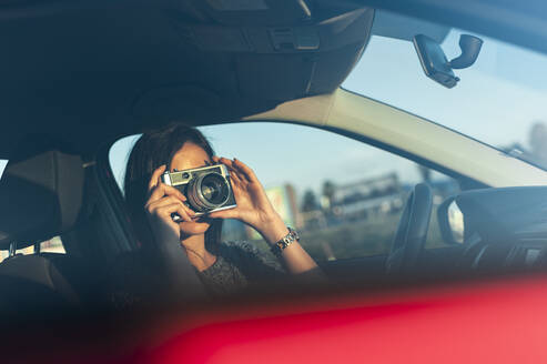 Junge Frau, die am Wochenende mit einer Filmkamera vom Auto aus fotografiert - JMPF00870