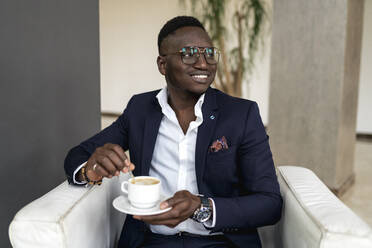 Smiling male professional looking away while holding coffee cup in hotel lobby - EGAF01612