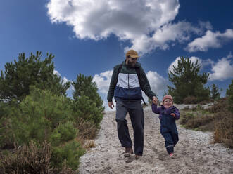 Lächelnder Vater und lächelnde Tochter gehen auf Sand gegen den Himmel - LAF02652