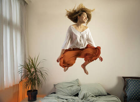 Happy young woman jumping over bed at home - AXHF00135