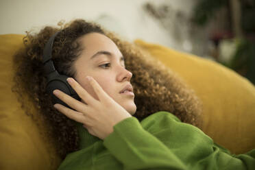 Young woman listening music through headphones while lying on bed at home - AXHF00144