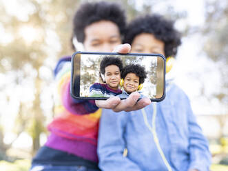 Smiling girl taking selfie with boy through mobile phone while sitting at park - JCCMF00961
