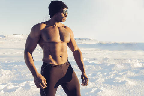 Muscular build sportsman looking away while standing in snow stock photo