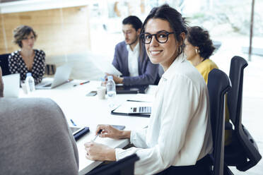 Lächelnde Geschäftsfrau, die mit ihren Kollegen im Sitzungssaal eines Coworking Centers sitzt - JSRF01318