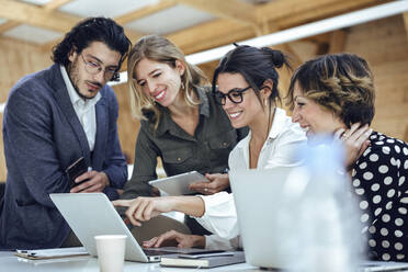 Smiling professionals discussing over laptop at office - JSRF01326