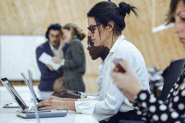 Businesswoman using laptop while sitting amidst colleagues in coworking office - JSRF01327