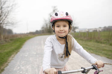 Lächelndes Mädchen auf dem Fahrrad mit Fahrradhelm - KMKF01475