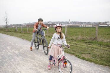 Brother and sister with bicycles on road against clear sky - KMKF01476