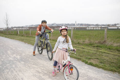 Bruder und Schwester mit Fahrrädern auf der Straße gegen den klaren Himmel - KMKF01476
