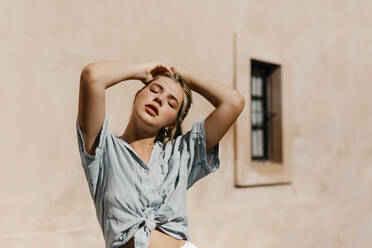 Schöne Frau mit Händen in den Haaren an der Wand stehend an einem sonnigen Tag - TCEF01501