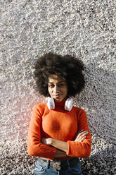 Afro woman with arms crossed and headphones standing against wall - XLGF01051