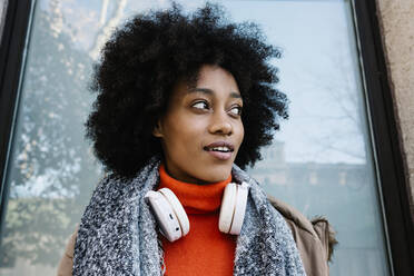 Afro-Frau mit Kopfhörern, die nachdenklich gegen eine Glaswand lehnt - XLGF01055