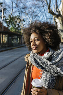 Afro-Frau mit Einweg-Kaffeebecher schaut weg, während sie an einem sonnigen Tag auf der Straße steht - XLGF01056