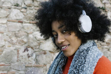 Afro junge Frau hört Musik durch Kopfhörer gegen Steinwand - XLGF01062