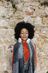 Afro woman with eyes closed against stone wall - XLGF01066