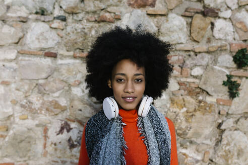 Junge Frau mit Kopfhörern in warmer Kleidung an einer Steinmauer - XLGF01067