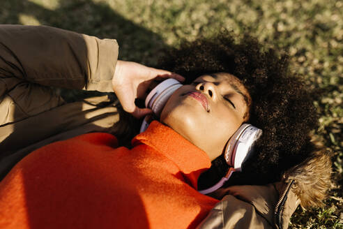 Afro-Frau mit geschlossenen Augen hört Musik auf Gras während des sonnigen Tages - XLGF01075