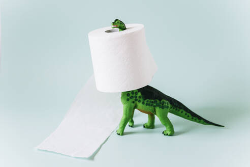 Diplodocus dinosaur toy with a roll of toilet paper around the neck on mint green background - GEMF04602