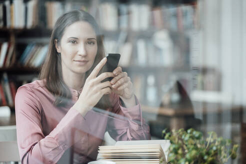 Unternehmerin mit Buch und Handy in der Hand schaut durch ein Glas in einem Cafe - JOSEF03064