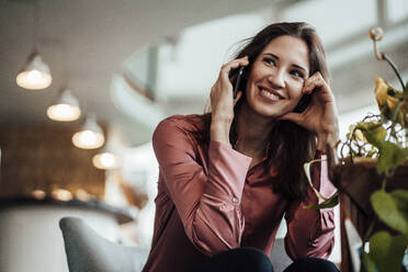 Lächelnde Geschäftsfrau, die wegschaut, während sie in einem Café mit ihrem Smartphone telefoniert - JOSEF03066