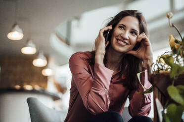 Smiling businesswoman looking away while talking on smart phone in cafe - JOSEF03066