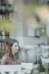 Geschäftsfrau mit Buch, die in einem Café mit ihrem Smartphone telefoniert - JOSEF03072