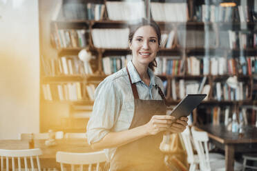 Lächelnde Managerin, die wegschaut, während sie ein digitales Tablet in einem Café hält - JOSEF03082