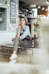 Weibliche Kellnerin sitzt auf den Stufen eines Cafés - JOSEF03090