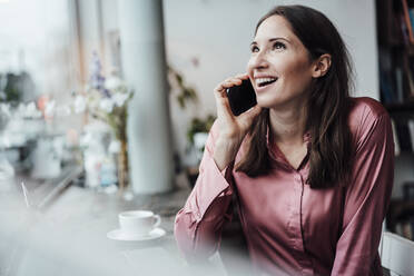 Lächelnde Unternehmerin, die mit ihrem Smartphone spricht und im Café nach oben schaut - JOSEF03093
