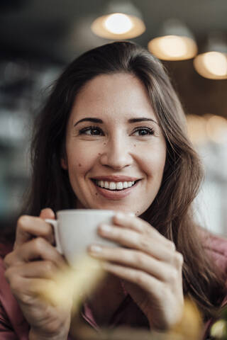 Glückliche Geschäftsfrau im mittleren Erwachsenenalter, die in einem Café Kaffee trinkt und wegschaut, lizenzfreies Stockfoto