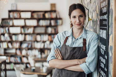 Female manager with arms crossed leaning by wall at cafe - JOSEF03120