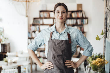 Confident female manager with hand on hip standing in cafe - JOSEF03123