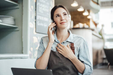 Weiblicher Besitzer, der mit seinem Smartphone telefoniert, während er in einem Café arbeitet - JOSEF03131