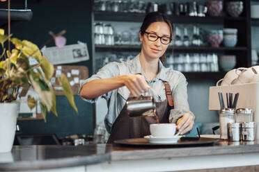 Weibliche Besitzerin gießt in einem Café Kaffee in eine Tasse - JOSEF03133