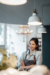 Smiling female manager with arms crossed in illuminated cafe - JOSEF03138