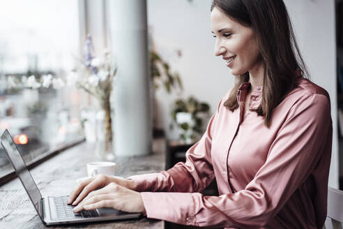 Lächelnde weibliche Fachkraft arbeitet am Laptop am Tisch im Café - JOSEF03144