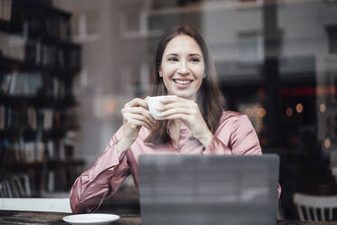 Lächelnde Unternehmerin, die in einem Café Kaffee trinkt und durch ein Glas schaut - JOSEF03148